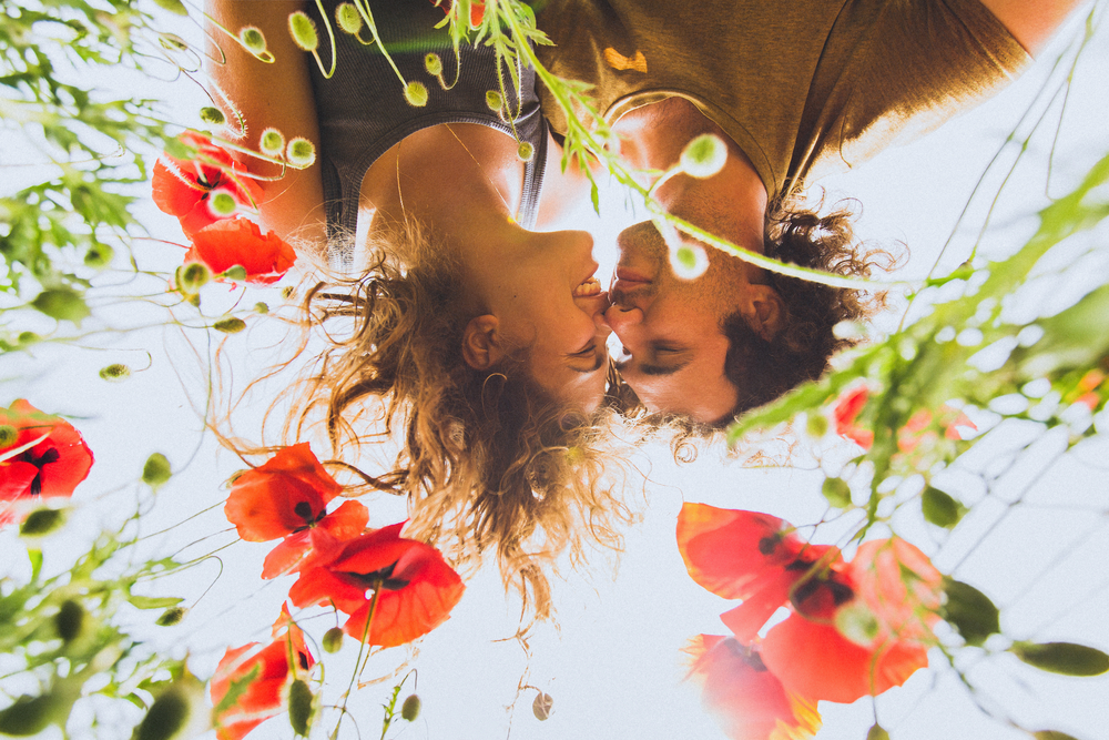 Young happy couple with curly hair enjoying in bright red and yellow blossoming field of poppies in spring