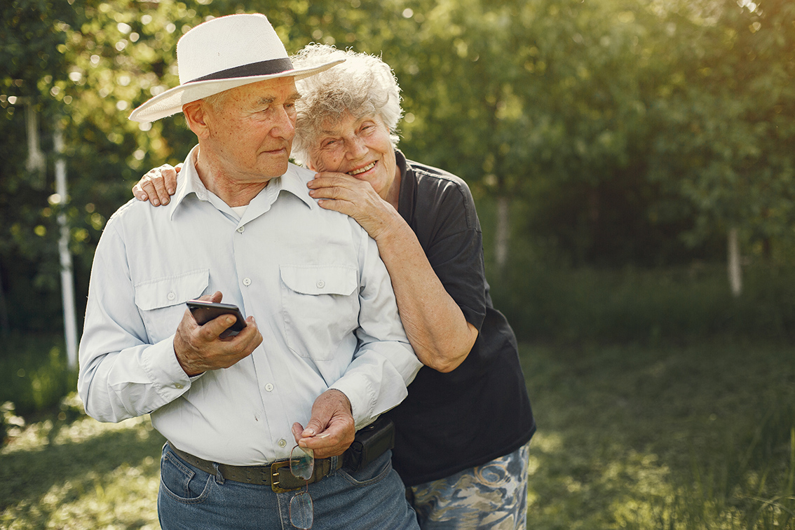 Adult couple in a summer garden. Handsome senior in a white shirt. Woman in a black blouse.